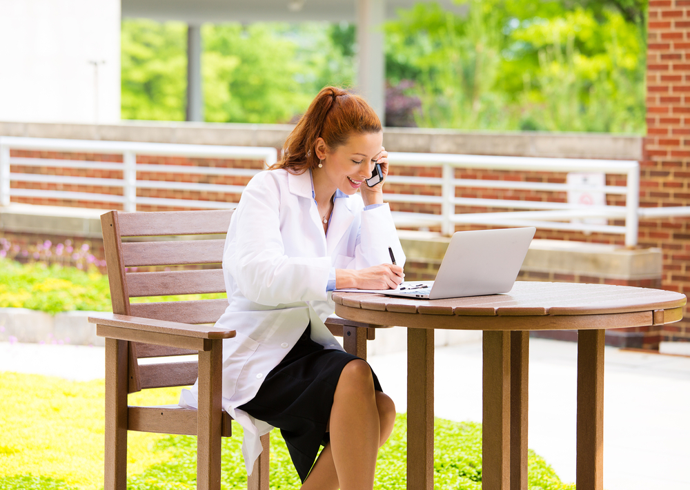 Closeup portrait, young smiling confident female doctor, healthcare professional talking on phone, giving consultation isolated background hospital park. Patient visit health care. Positive emotions