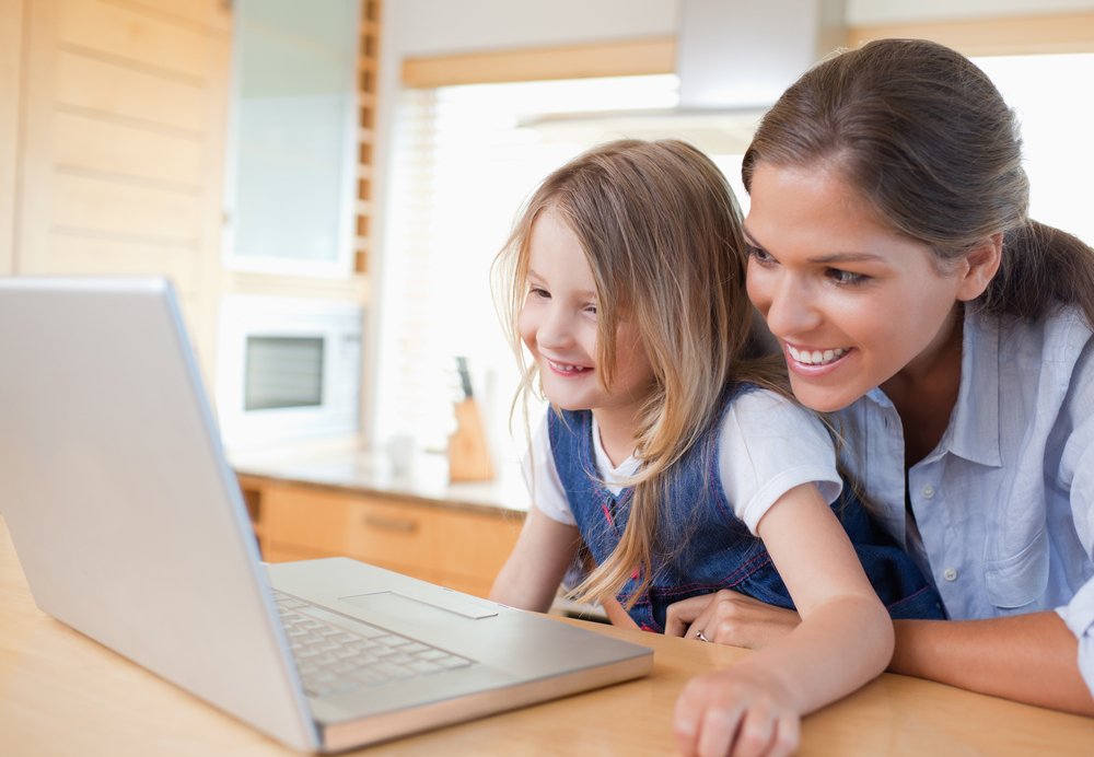 Smiling mother and her daughter using a notebook in their kitchen